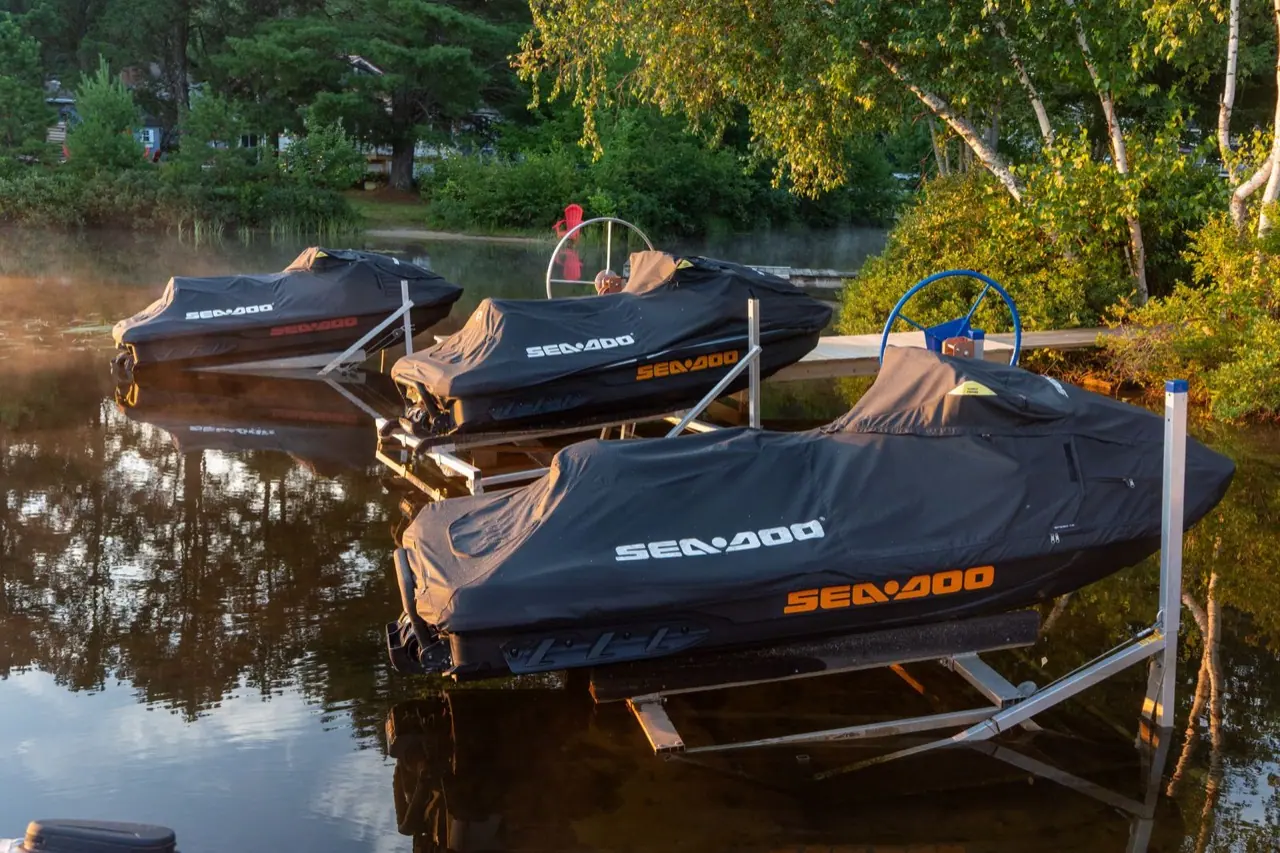 Three personal watercraft under covers at a lake dock
