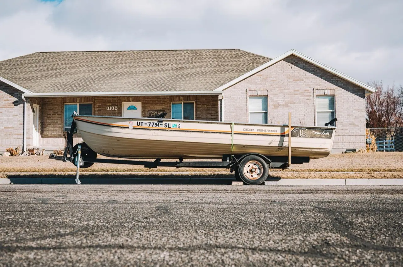 A fishing boat on its trailer parked in a suburban driveway